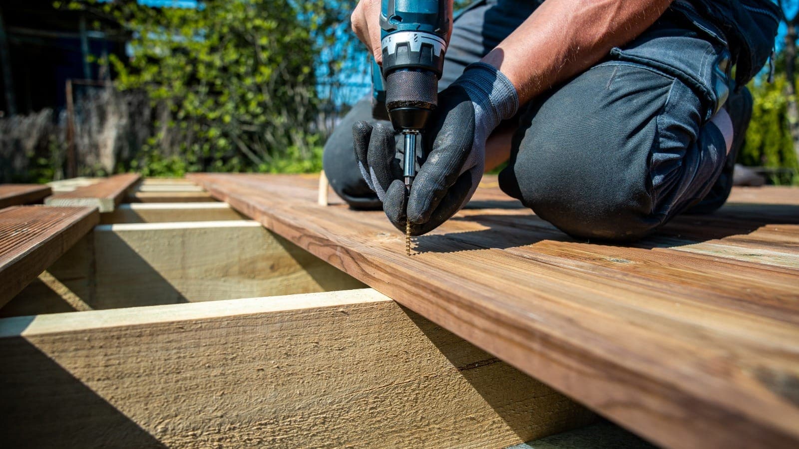 Gloved hands using a cordless drill to fasten decking timber outdoors
