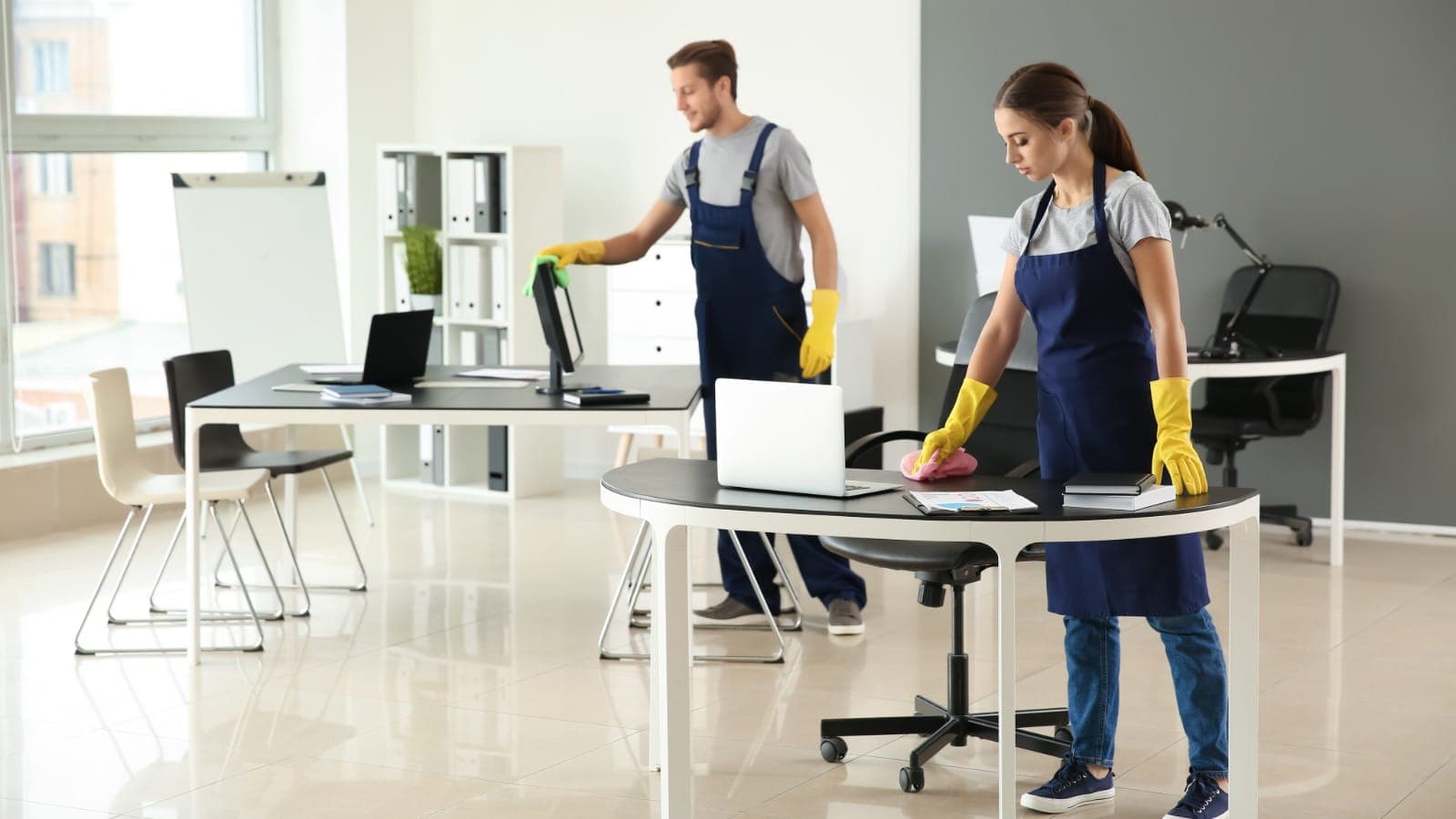 Two commercial cleaners wiping desks in an after-hours office