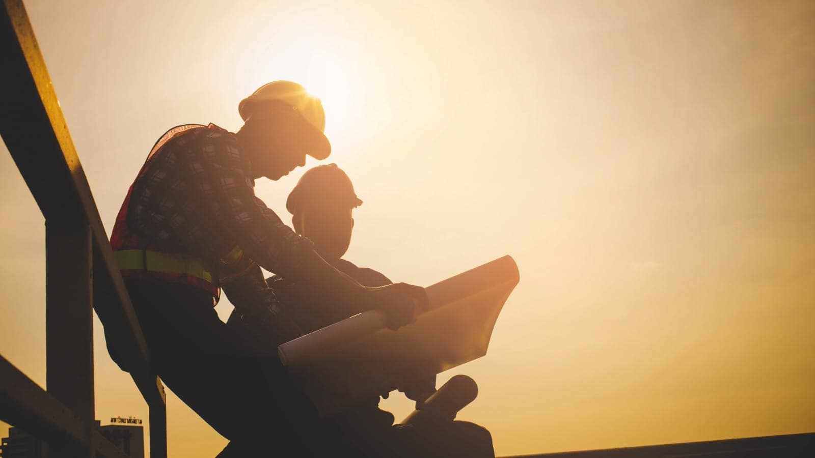 Two construction workers silhouetted against a sunset reviewing site plans