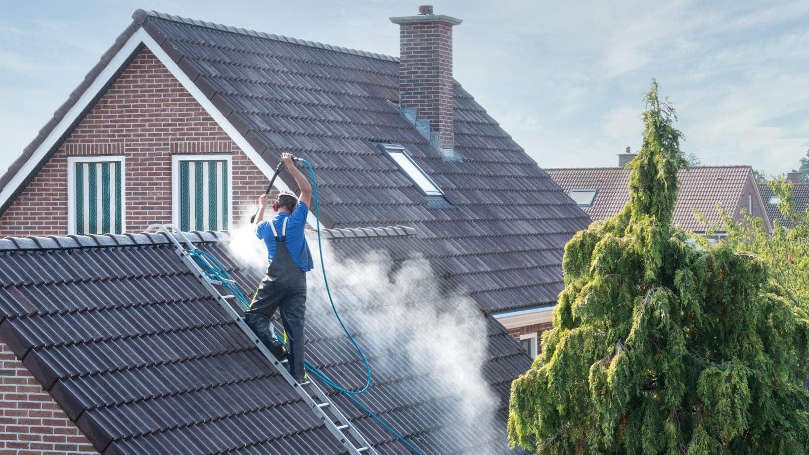 Tradesperson using a water blaster on weatherboard cladding