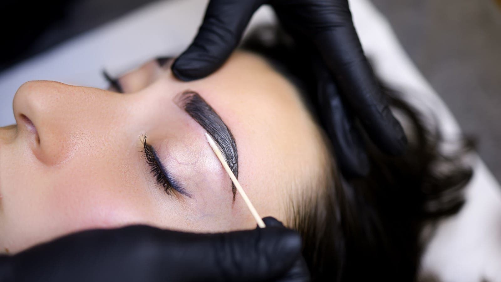 Brow specialist applying tint to a client's eyebrow with a wooden applicator