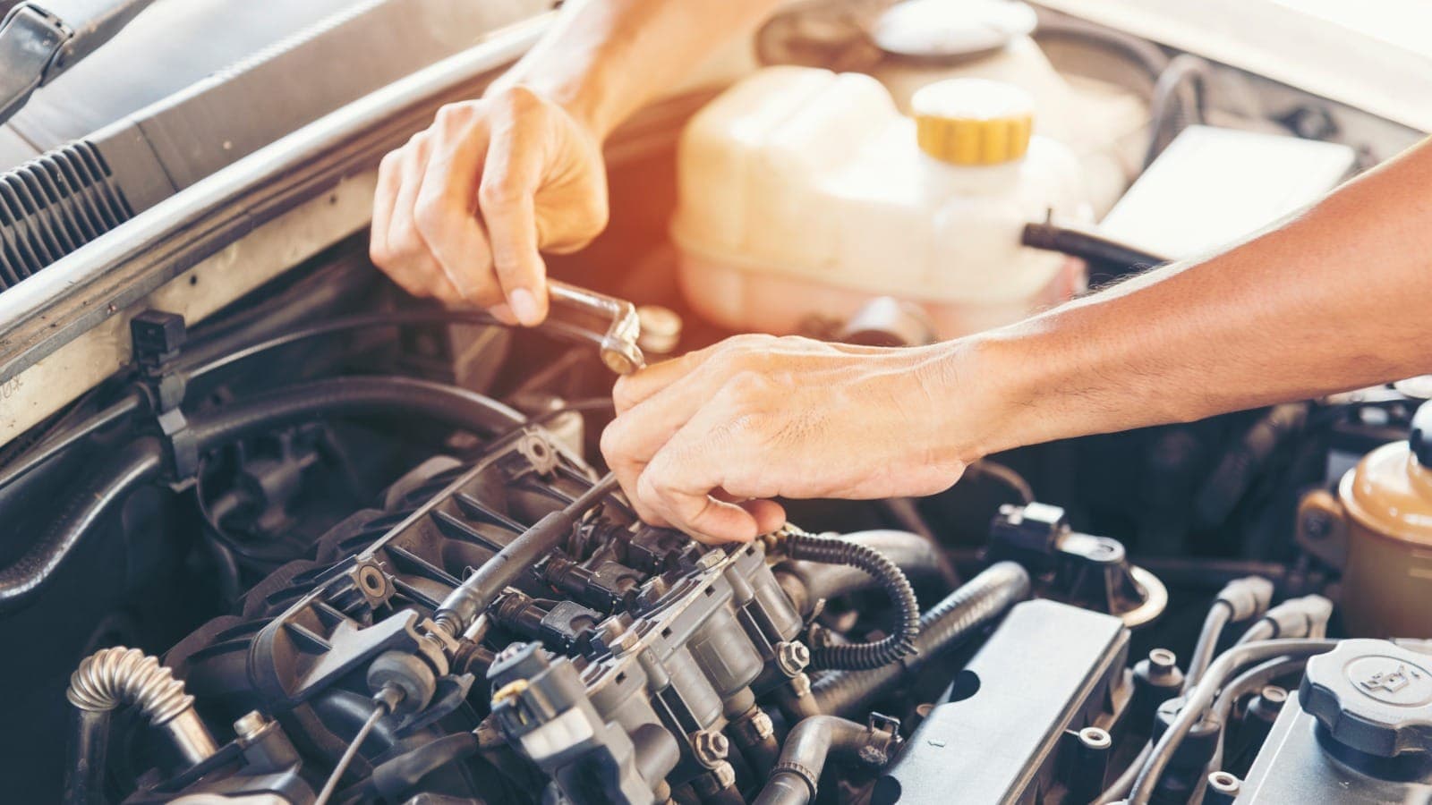 Hands tightening a bolt on a car engine with the bonnet open