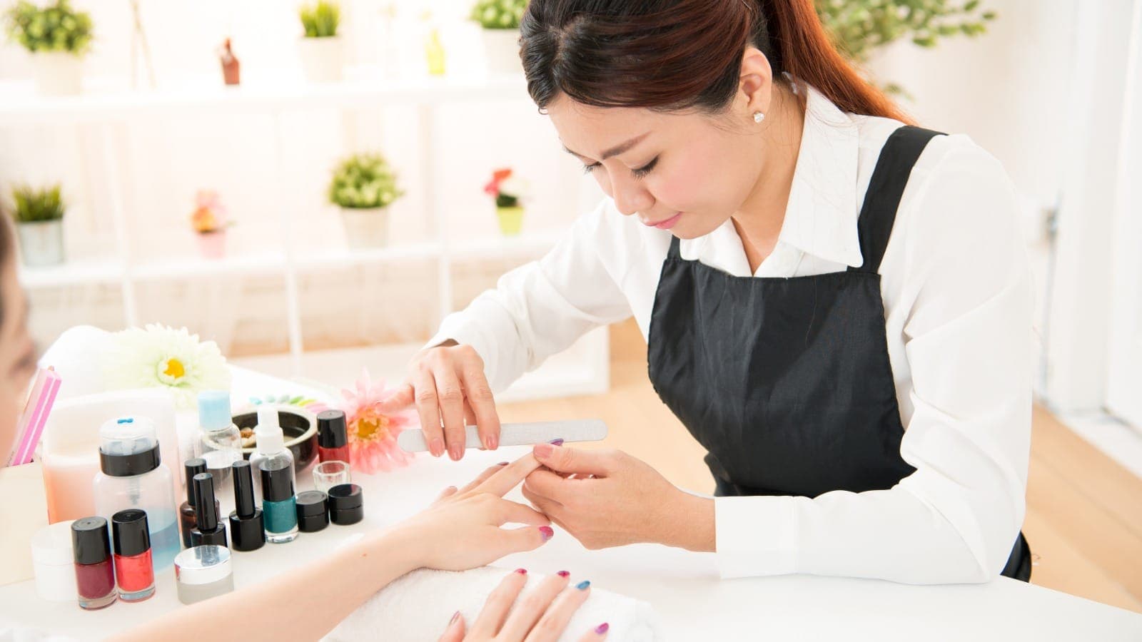 Nail technician filing a client's nails with polish bottles on the table