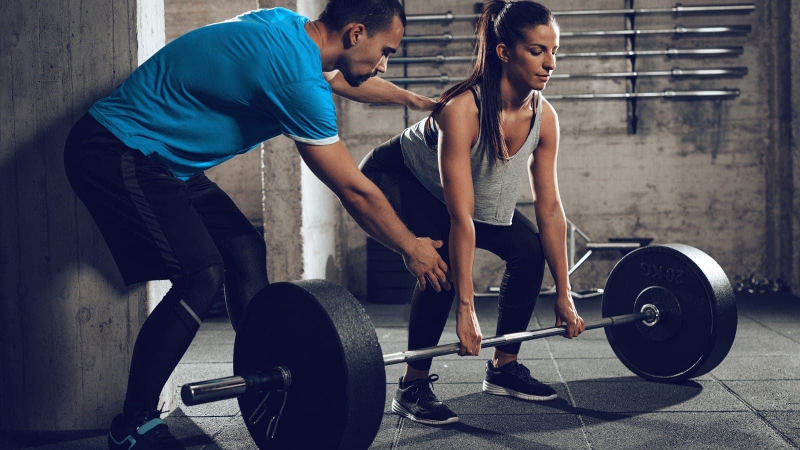 Personal trainer coaching a client through a barbell deadlift in a gym