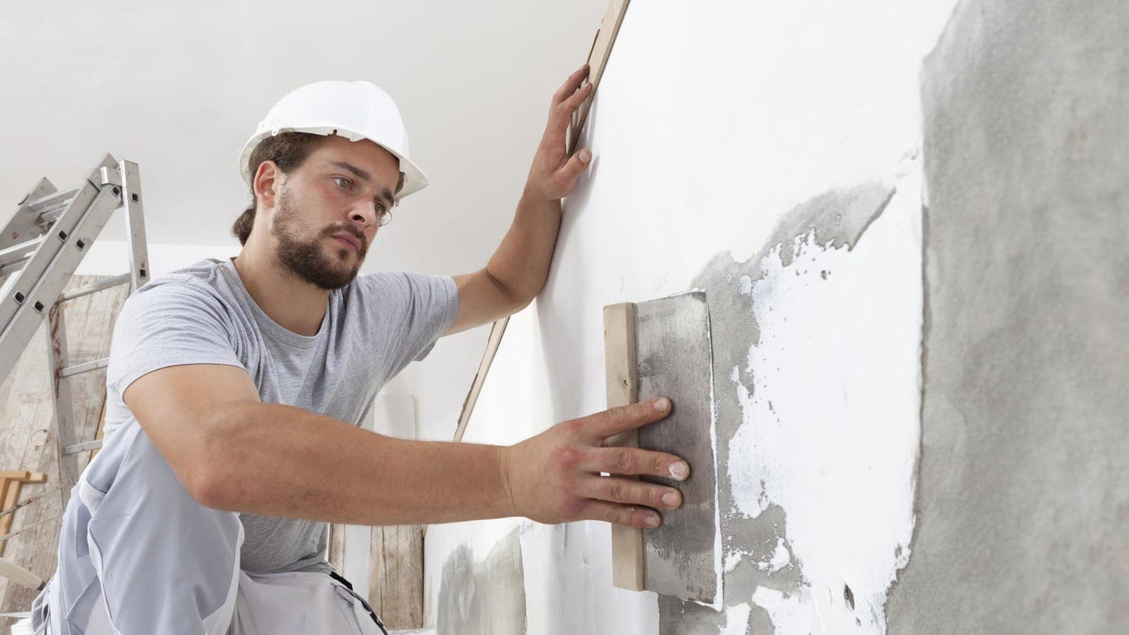 Plasterer in a hard hat smoothing a wall with a wooden float trowel