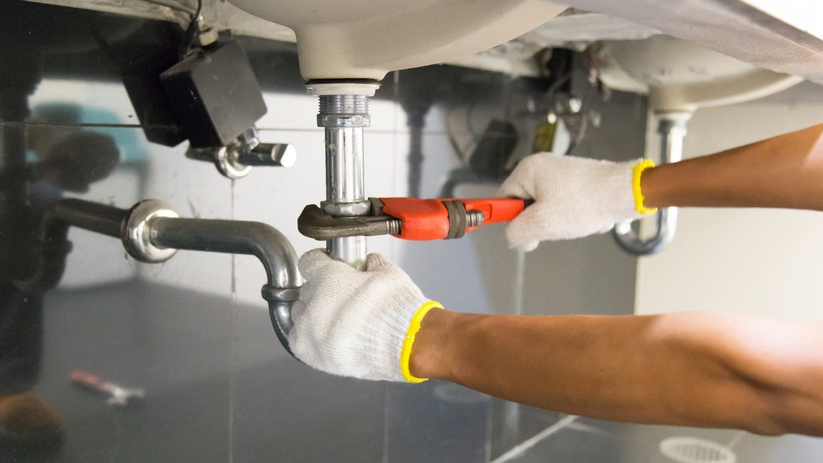 Plumber using a pipe wrench under a residential sink