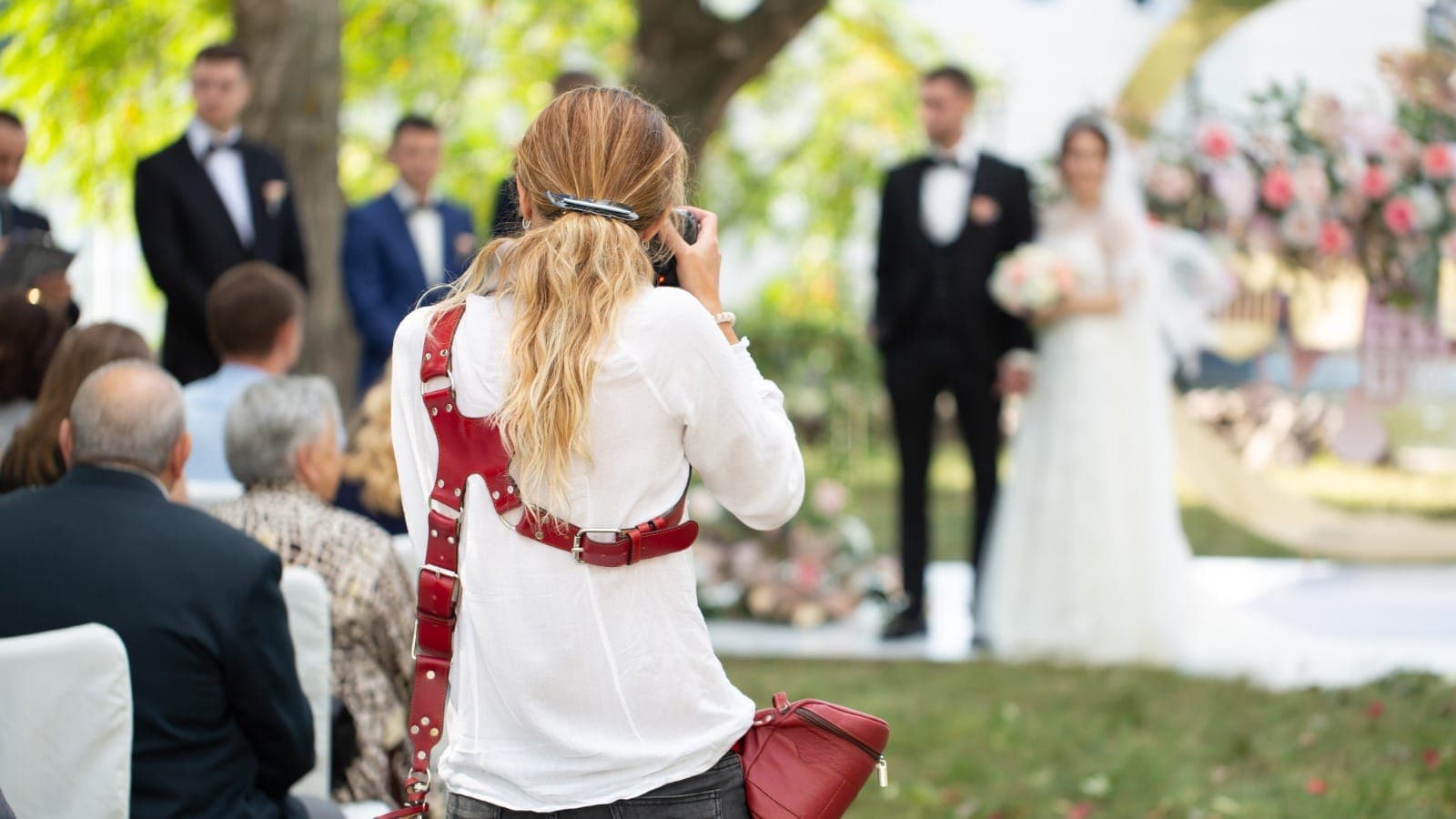 Wedding photographer with red camera harness shooting a ceremony