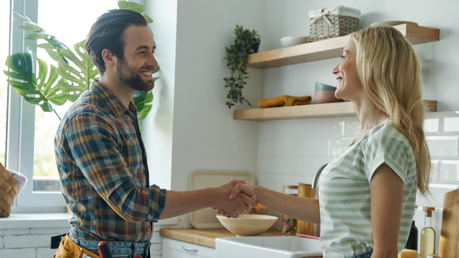 Tradesperson with a tool belt shaking hands with a homeowner in a residential kitchen