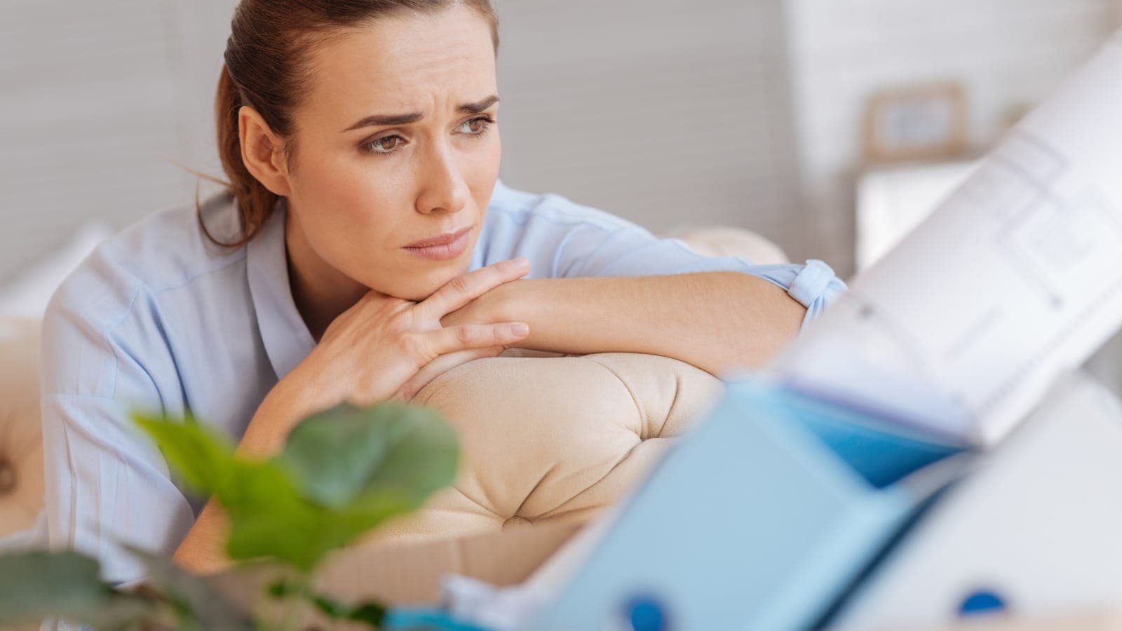 Woman at home looking thoughtfully into the distance with a blueprint in soft focus